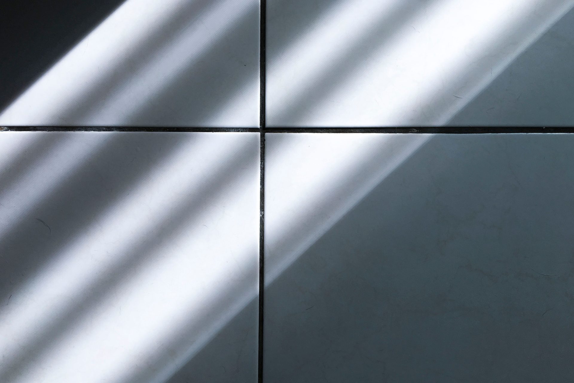 Ein minimalistisches Bild, das Sonnenlicht einfängt, welches Schatten auf einen Fliesenboden wirft.